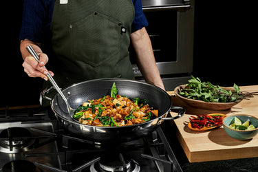 A person cooking meat and vegetables in a HexClad hybrid pan.