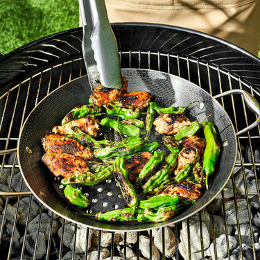 Chicken wings and green peppers being sauted in the HexClad 12" Hybrid BBQ Grill Pan on top of a grill