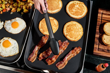 A person cooking eggs, pancakes, and bacon on the HexClad Double Burner Griddle.
