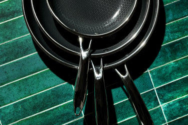 Three HexClad pans stacked on top of each other on an emerald green, tiled surface.
