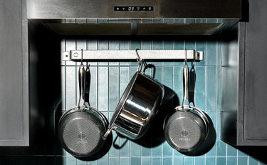 Pots and pans hanging from a rack against kitchen tile backsplash.