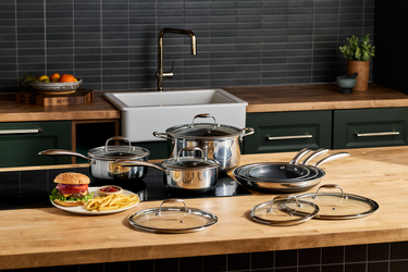A 12-piece HexClad pots and pans set arranged on a kitchen countertop, along with a plate of a hamburger and fries.