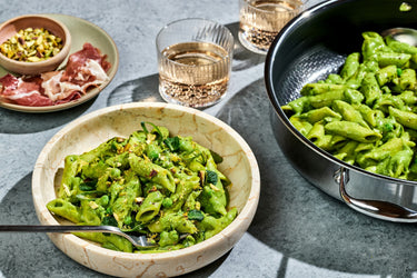 A bowl of HexClad’s creamy pea and mint puree pasta, next to a pot and two glasses.