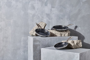 A 3-piece HexClad frying pan set presented on a minimalist, grey stone setting.