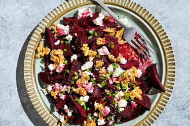 Salad of red beets with nuts and feta on a ridged plate.
