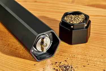 HexClad HexMill pepper grinder laying on wood surface with cap full of ground pepper next to it