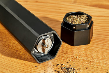 HexClad HexMill pepper grinder laying on wood surface with cap full of ground pepper next to it