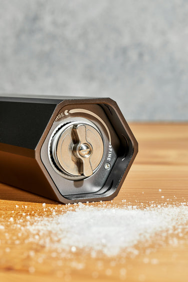 A heavy duty HexClad HexMill salt grinder with salt on wood surface.