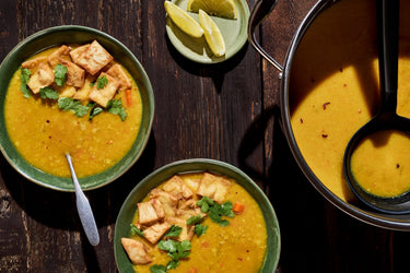 yellow tofu dal in two bowls next to a large stock pot
