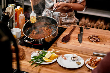 A person cooking on a glass stove using a HexClad pan, with many ingredients next to them on the counter.