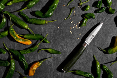 A small HexClad knife surrounded by green and yellow peppers.