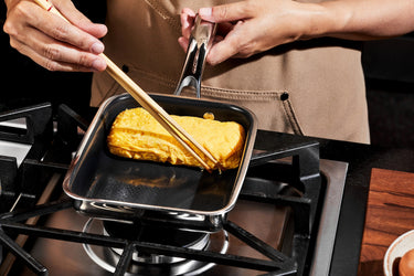 A person making a Japanese omelette in a square pan.
