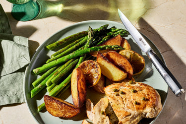 A plate of asparagus, roasted potatoes, chicken, and lemon.