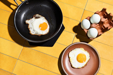 A fried egg in a HexClad pan, and a fried egg on a plate, next to a carton of eggs,