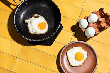A fried egg in a HexClad pan, and a fried egg on a plate, next to a carton of eggs,