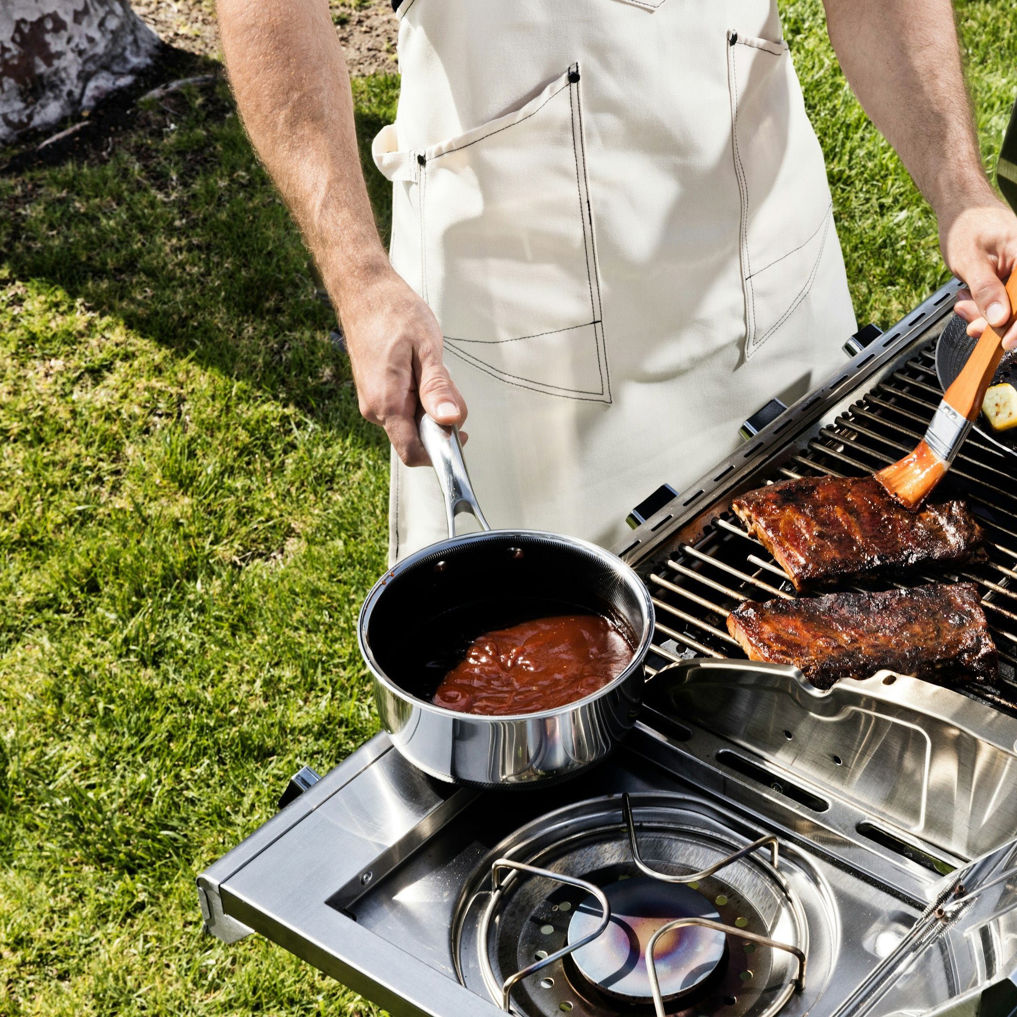 Person grilling ribs and basting with sauce in a yard.