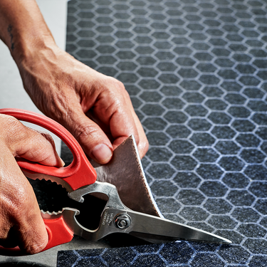 Hands cutting a HexClad Dish Drying Mat with a pair of red scissors.