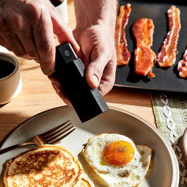 Hands grinding pepper on top of a fried egg, using HexClad