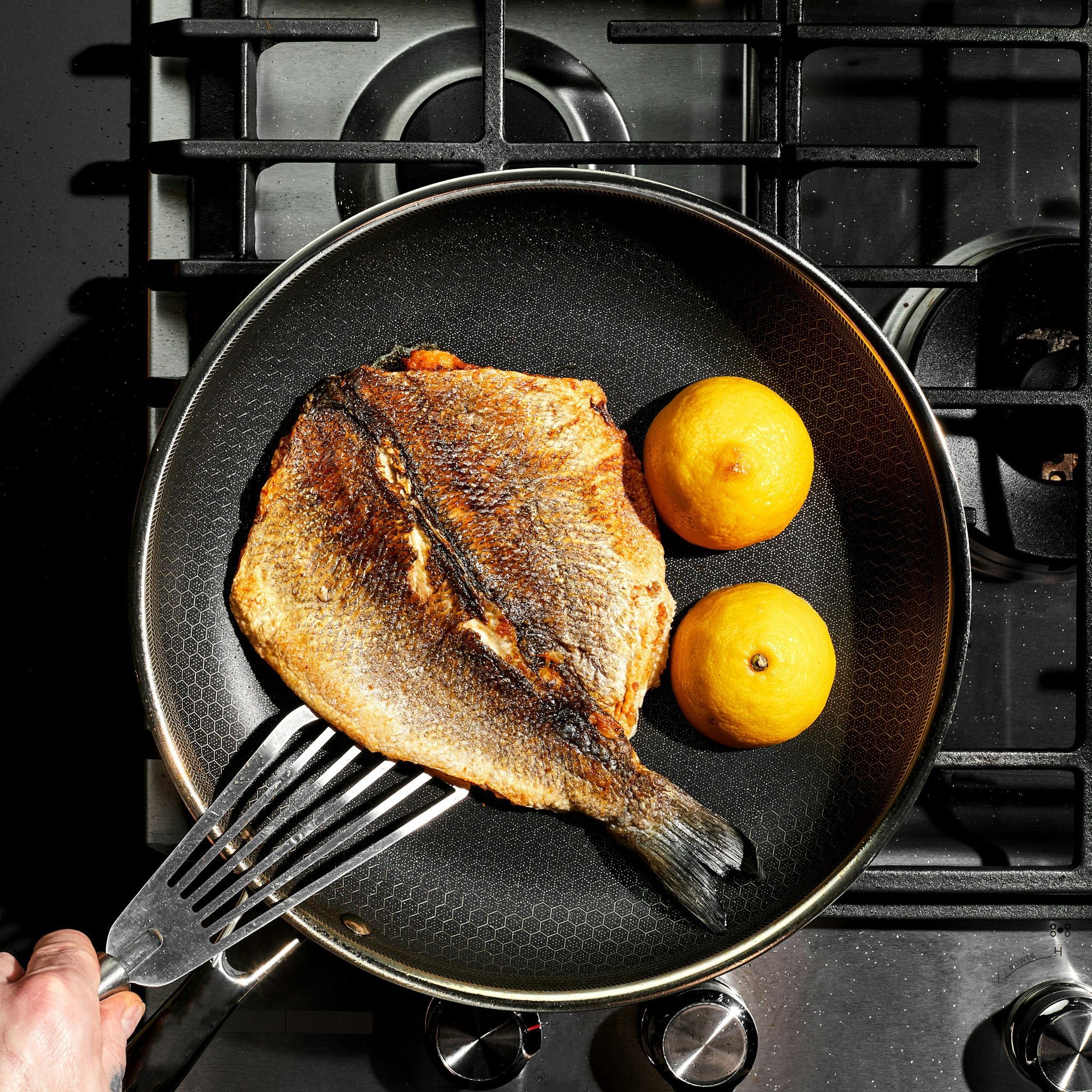 Fish fillet and lemons cooking in a pan on a stovetop.