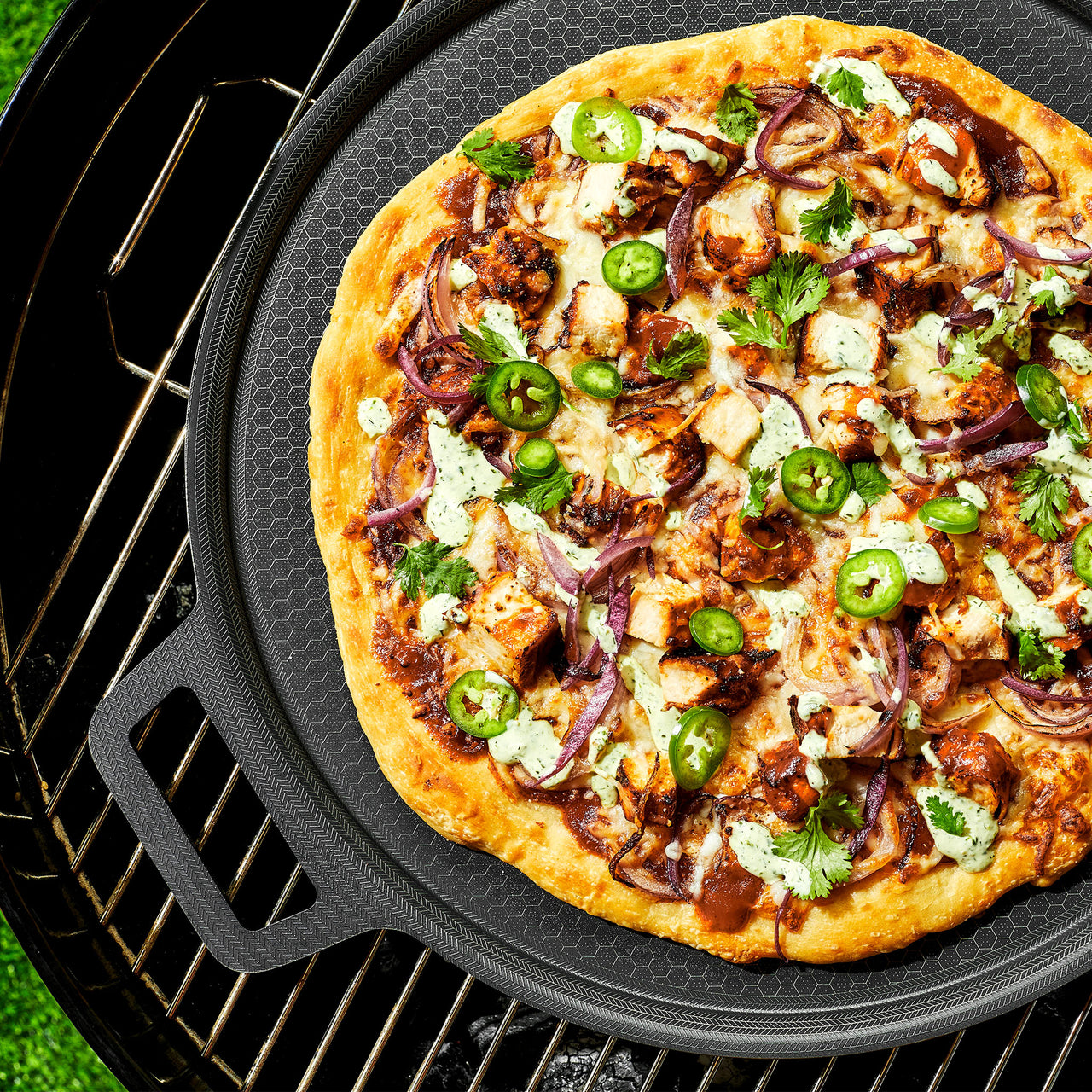 A pizza with veggies and chicken on the HexClad hybrid pizza steel, sitting on a grill
