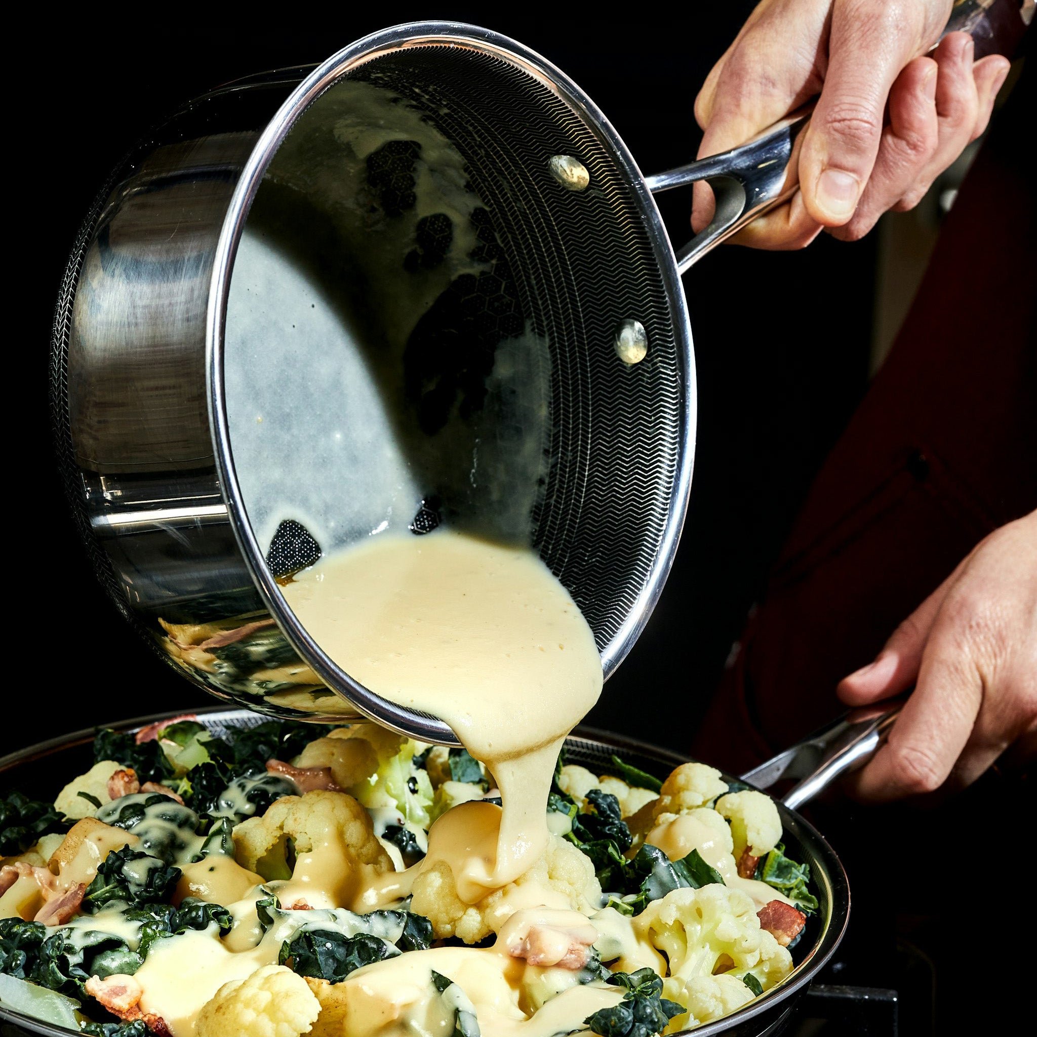 Pouring creamy sauce over vegetables from a pot.