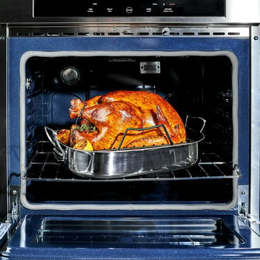 A turkey sitting inside the HexClad Hybrid Roasting Pan, along with herbs and lemon slices, being roasted in the oven.