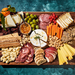 A charcuterie board of meats, cheeses, fruit, and spreads on a wooden cutting board.