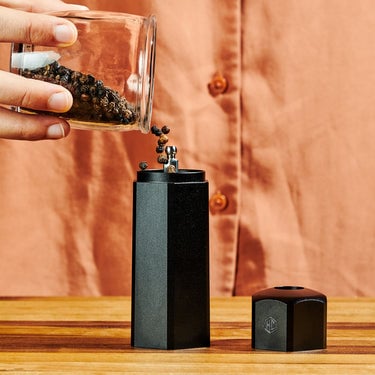 Hands pouring black peppercorns into the top of HexClad