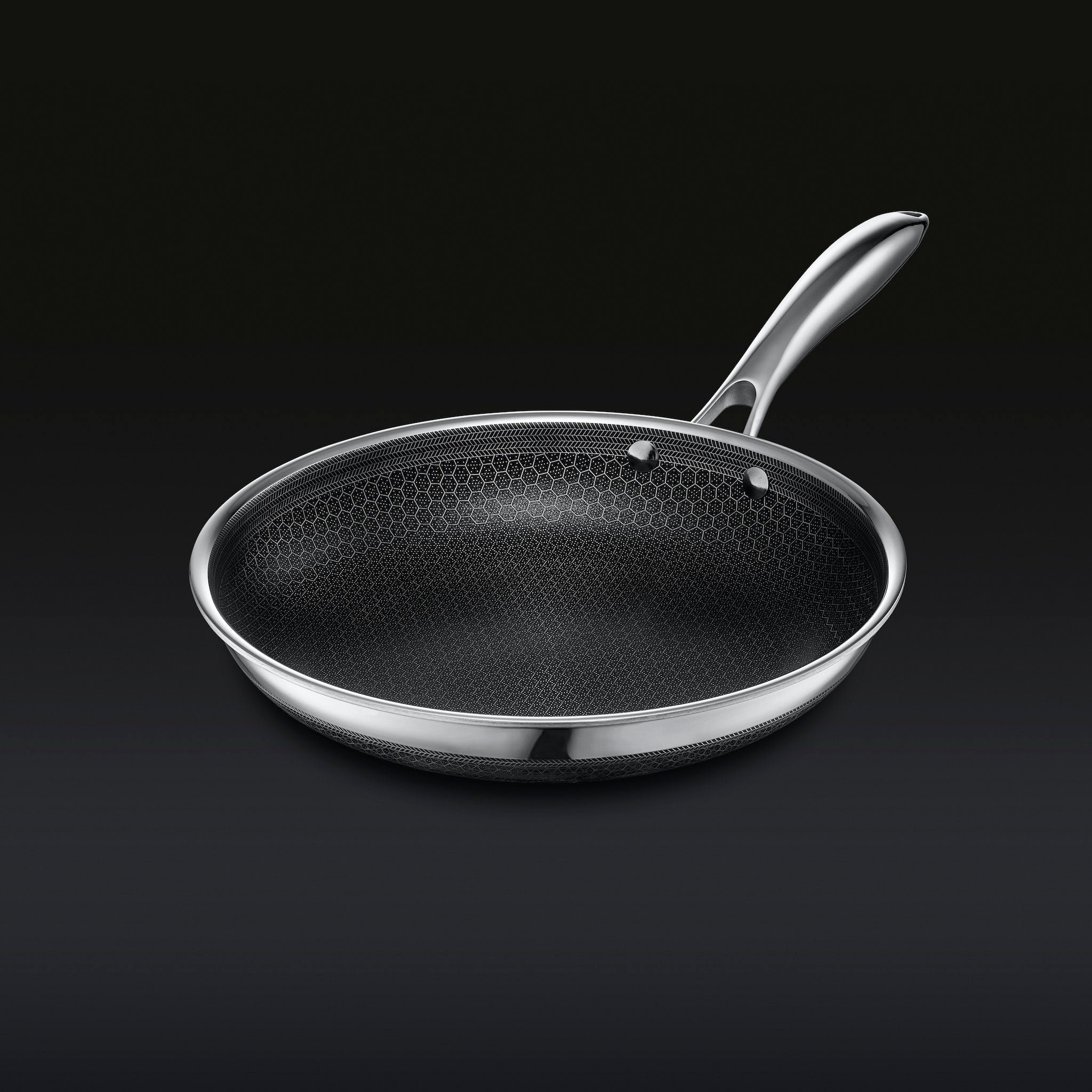 Stainless steel frying pan with a hexagonal pattern on a dark background.