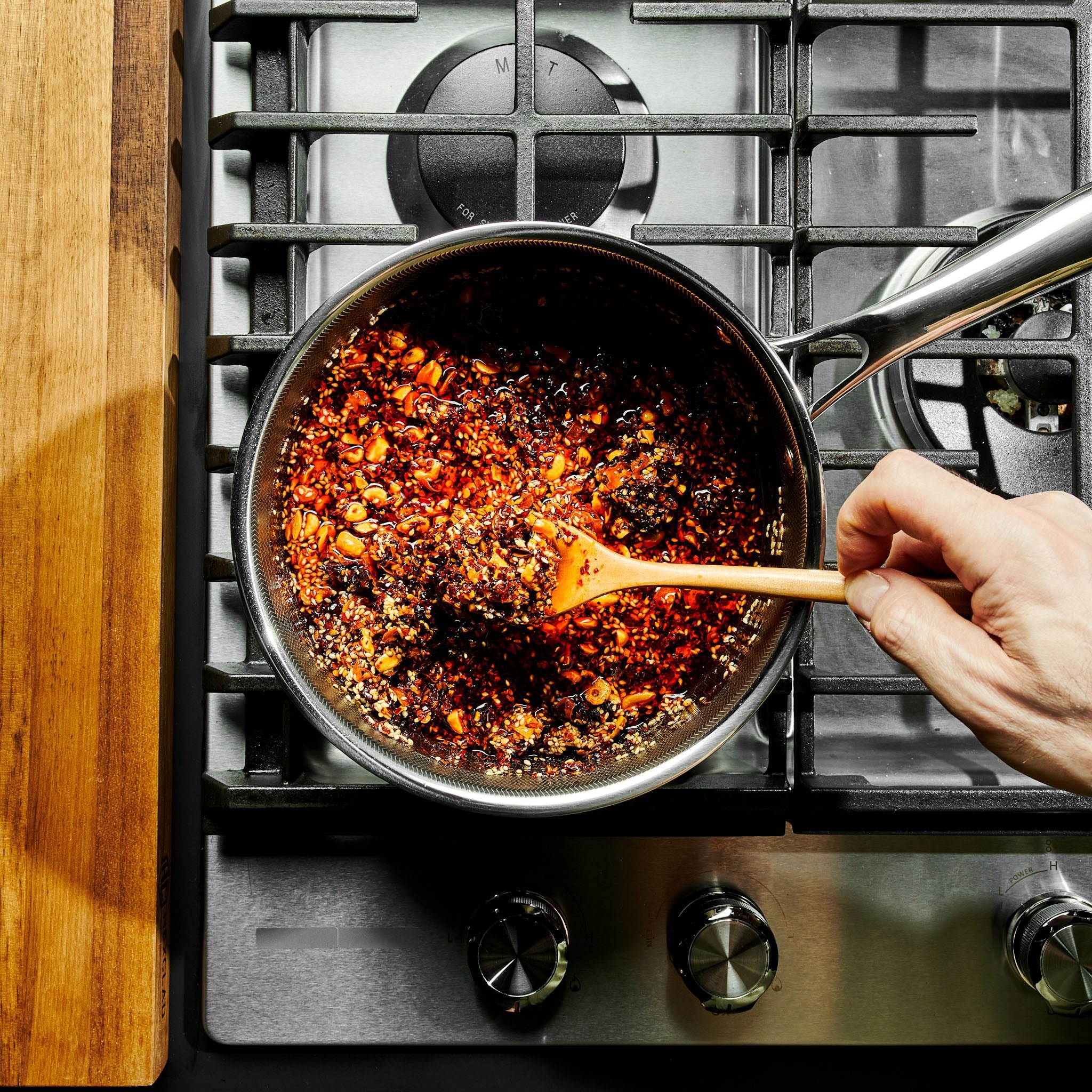Person stirring a mixture of spices and oil in a frying pan on a stovetop.
