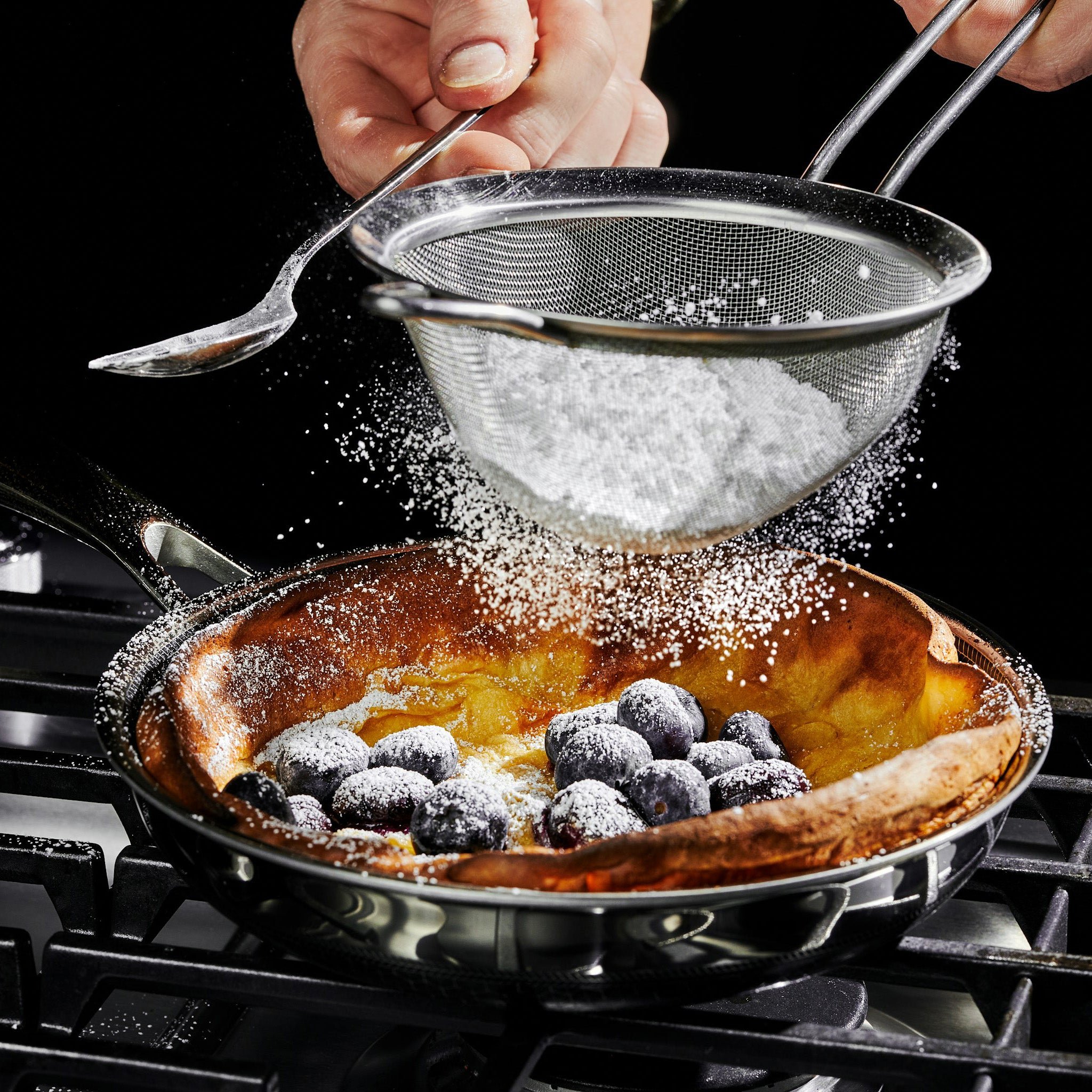 Sprinkling powdered sugar onto a Dutch baby pancake with blueberries.