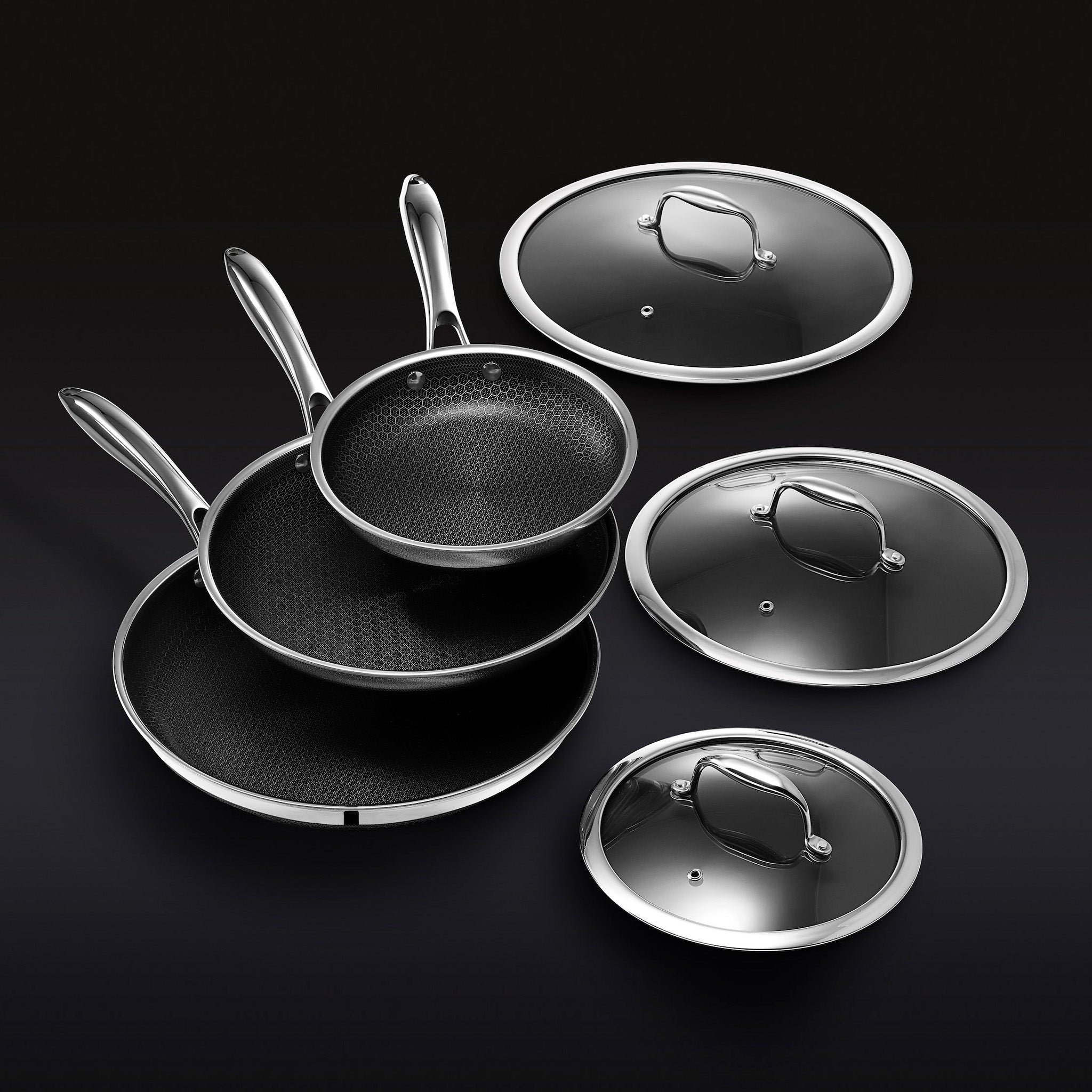 Stacked nonstick frying pans with three matching glass lids against a black background.