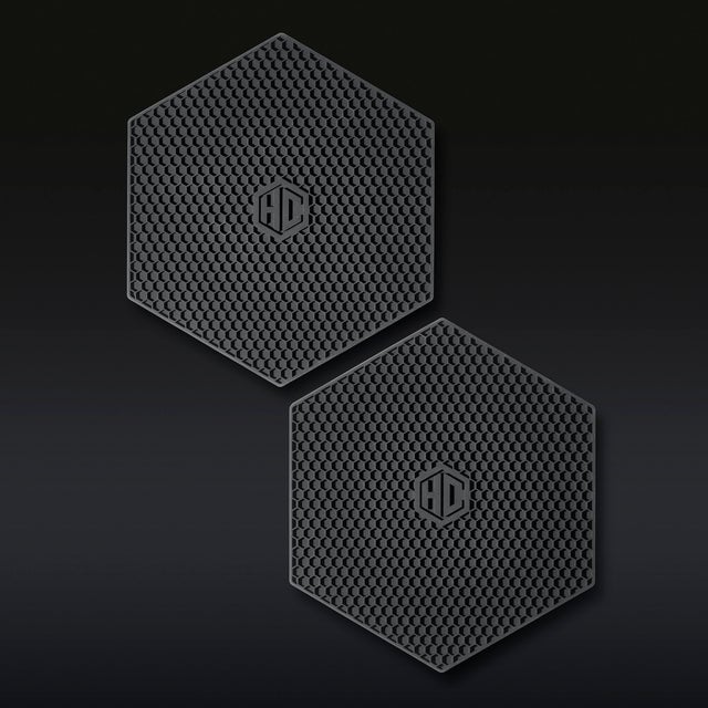 Two hexagonal textured black coasters with a logo at the center on a dark background.