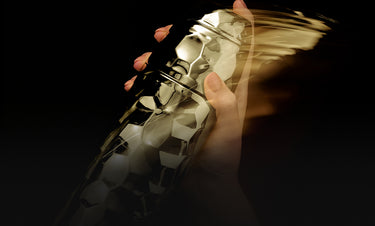 Gold sneaker held by a hand with pink nail polish against a dark background