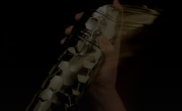 Close-up of a hand holding the gold cocktaial sneaker with black checkered pattern on a dark background