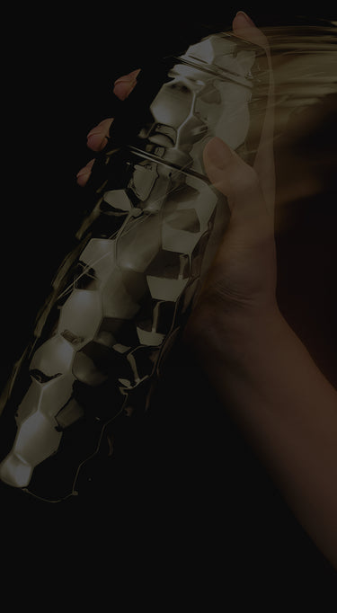 Close-up of a hand holding the gold cocktaial sneaker with black checkered pattern on a dark background