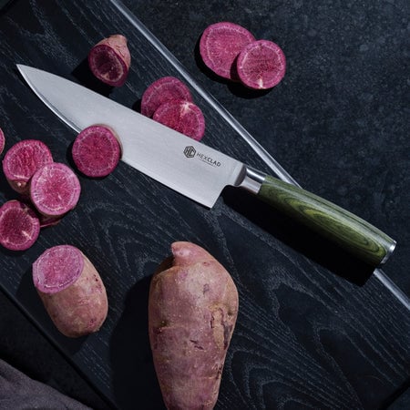 chef knife slicing vegetables on a black wooden cutting board