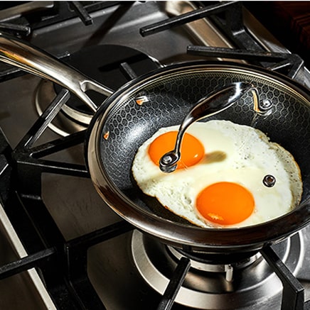 Two sunny-side-up eggs cooking in a frying pan on a stove.