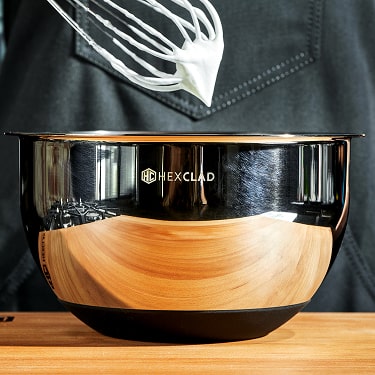 Stainless steel mixing bowl with a whisk above it, containing whipped cream.