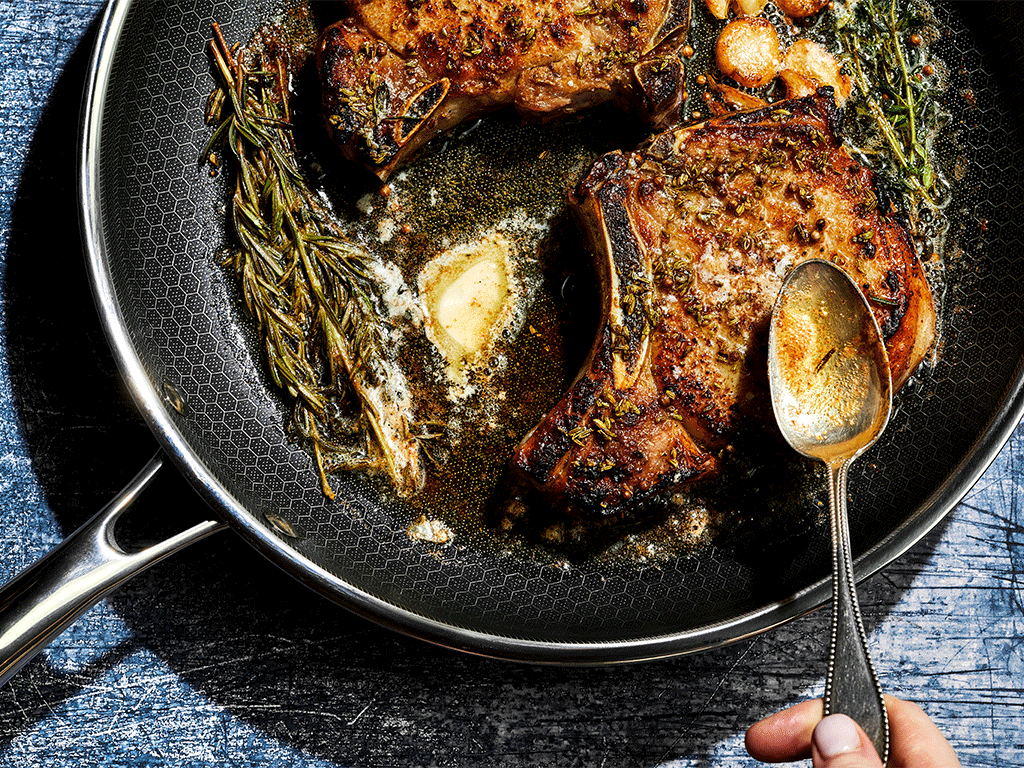 Two cooked pork chops in a pan with herbs and butter.
