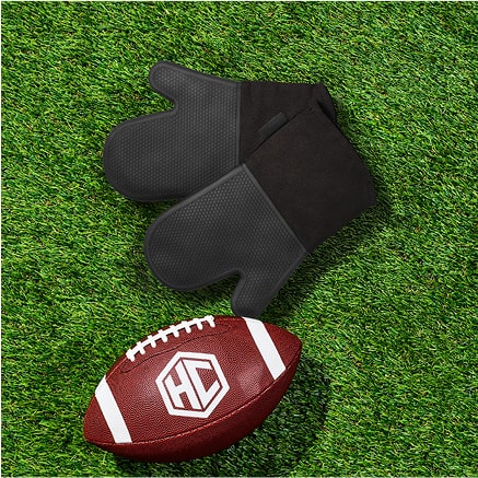 Football and black oven mitts on green grass.
