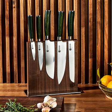 Set of kitchen knives in a wooden block on a countertop with herbs and citrus fruits.