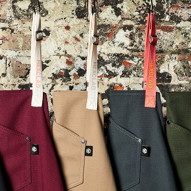 Four colorful aprons hanging against a textured brick wall.