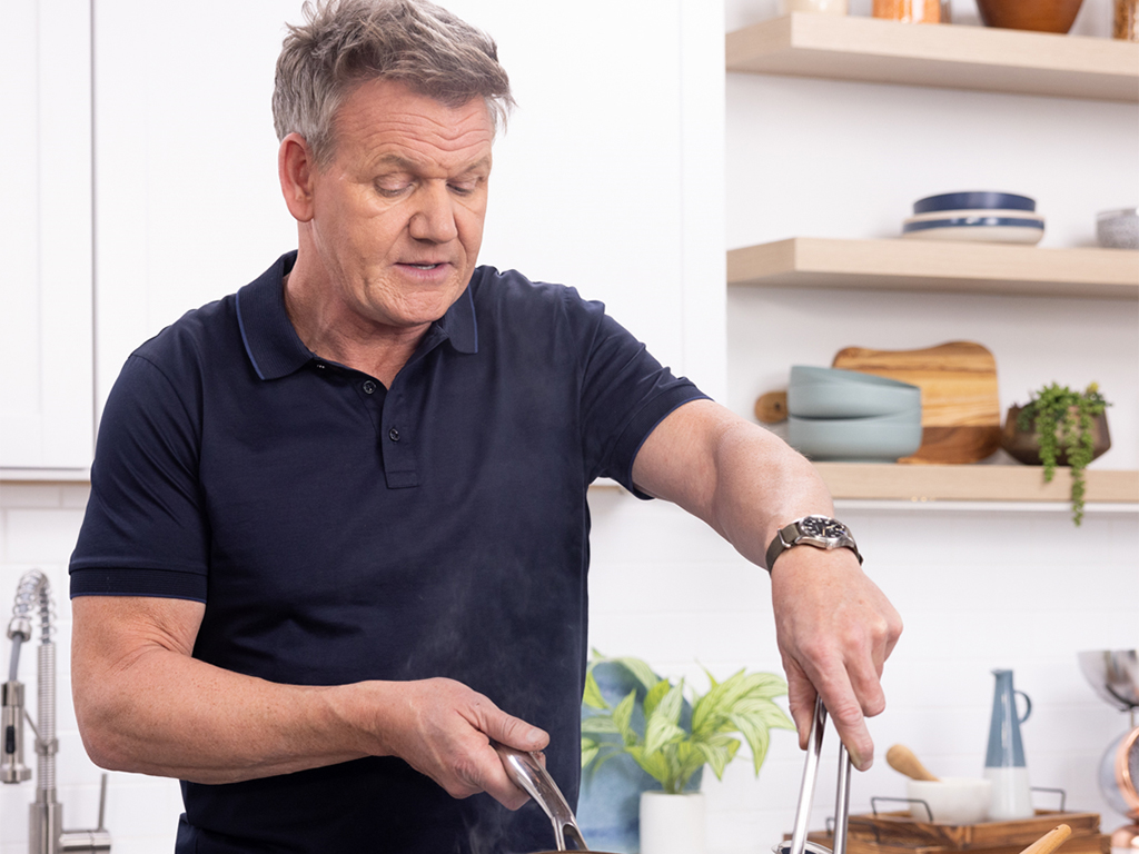 Person cooking in a kitchen with plants and shelves in the background.