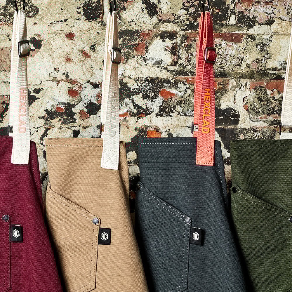 Four aprons of various colors hang against a rustic brick wall.