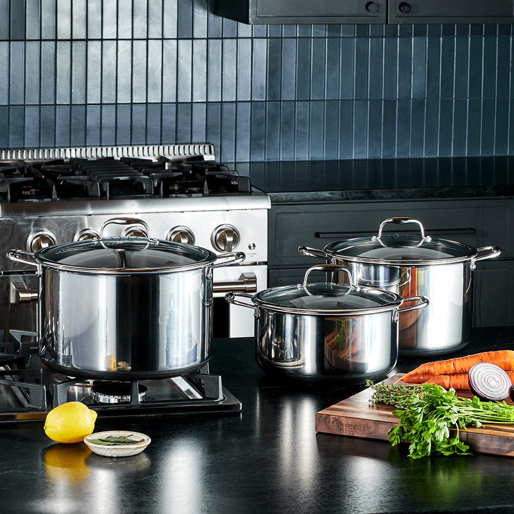 Stainless steel pots on stove with vegetables on counter in modern kitchen.
