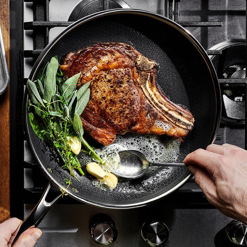 Cooking steak with herbs and garlic in a pan on the stove.