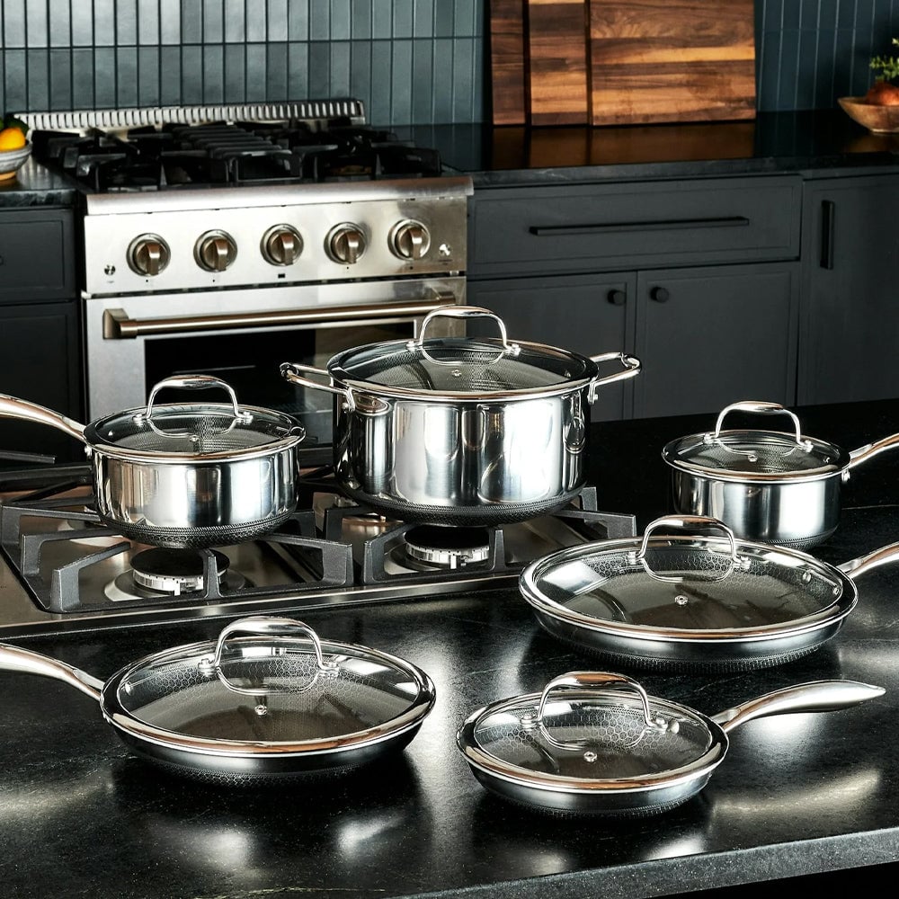Stainless steel cookware set with glass lids on a modern kitchen stove.