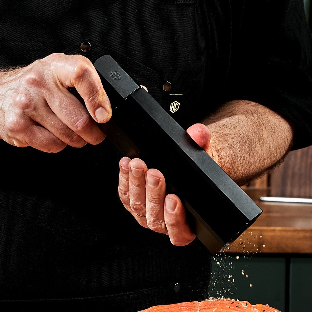 Person using a black mill to season food with salt.