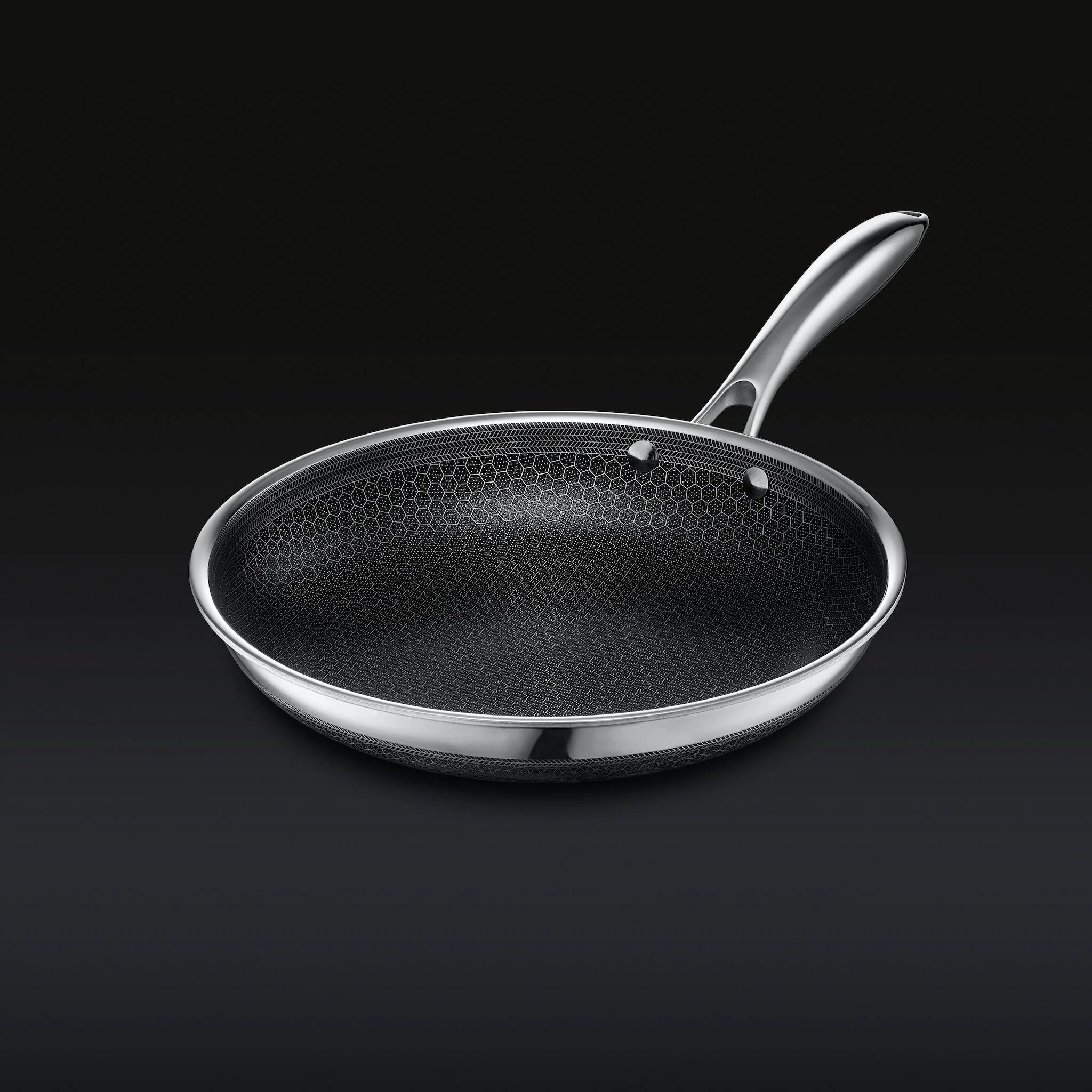 Stainless steel frying pan with a textured, honeycomb-patterned surface on a dark background.